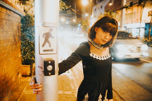 Woman in Black Clothes Standing by Post on Street at Night