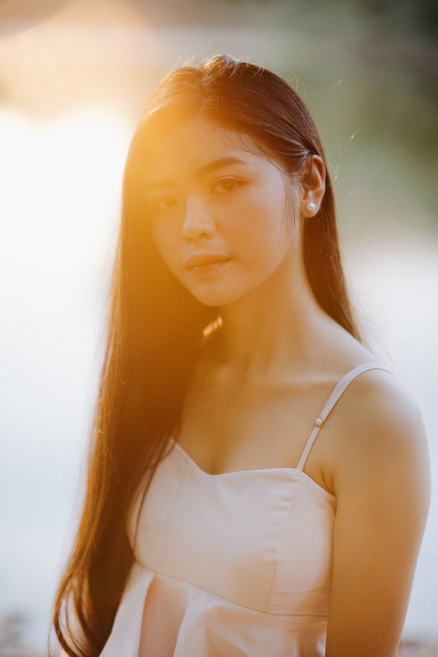 A serene portrait of an Asian woman with long hair captured during a warm sunset. Perfect for fashion and lifestyle them