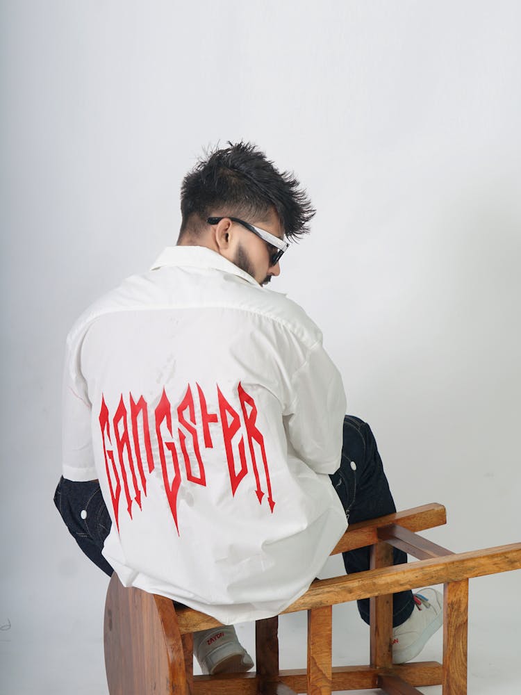 Model In A White Shirt With A Gangster Print On Back Sitting On An Overturned Stool