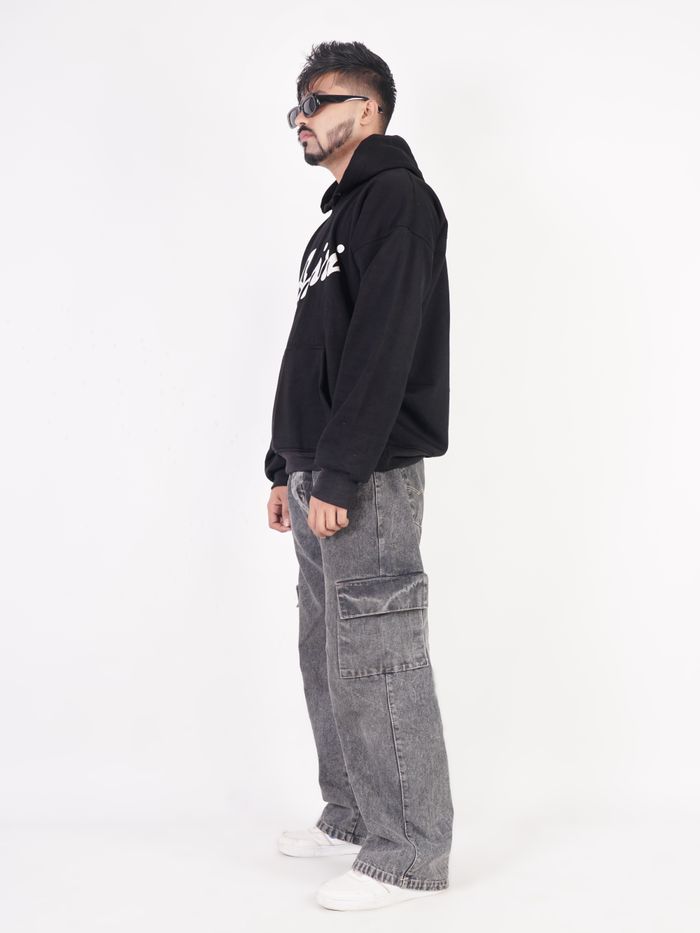 Side view of a model styled in a dark printed hoodie and trousers against a low-key backdrop