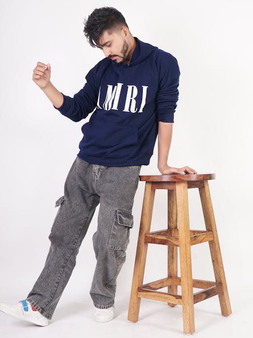 Model in a Navy Blue Printed Hoodie and Faded Black Denim Cargo Pants Leaning on a Wooden Stool