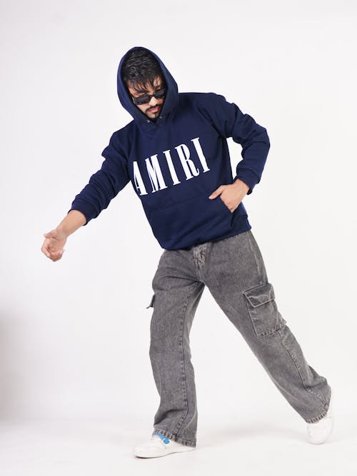 Model in a Navy Blue Hoodie with the AMIRI Print and Faded Black Denim Cargo Pants