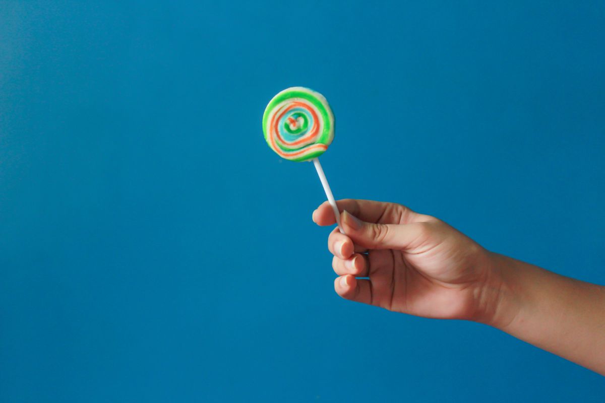 Close-up of a hand holding a colorful lollipop with a blue background, perfect for candy-related themes.