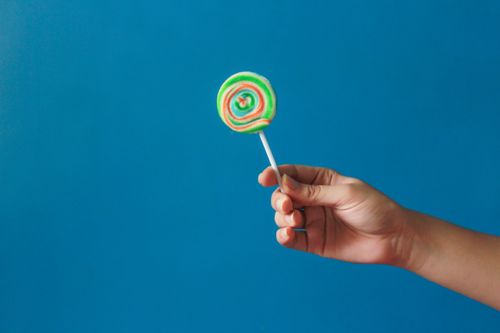 Free Close-up of a hand holding a colorful lollipop with a blue background, perfect for candy-related themes. Stock Photo
