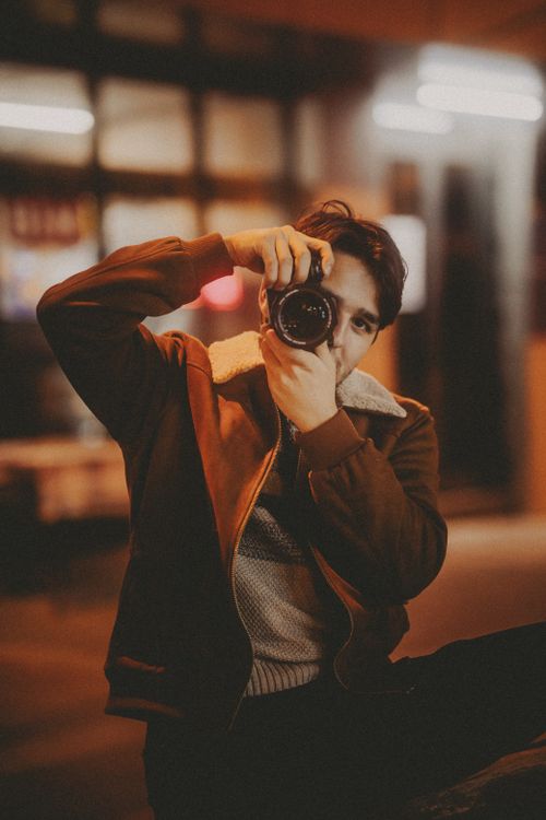 Free A man takes nighttime photography in an urban setting, capturing vibrant city life. Stock Photo