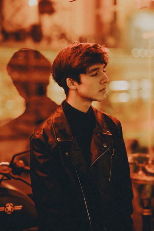Free Stylish portrait of a young man in a leather jacket, set against a moody city backdrop at night. Stock Photo