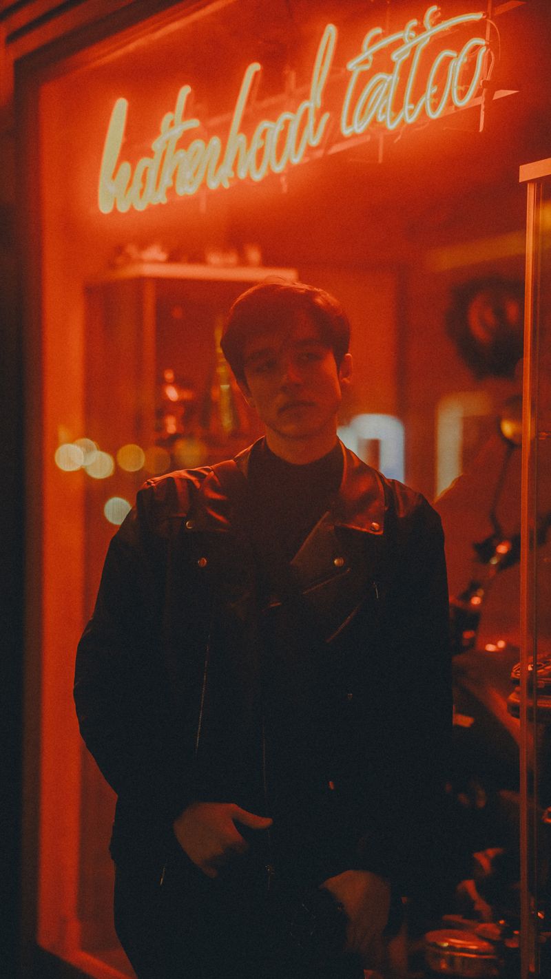 Man in a leather jacket lit by neon street signs at night — UMUT RAW on Pexels