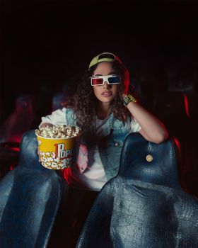 A woman in 3D glasses holds popcorn in a cinema setting, creating a fun movie night vibe.