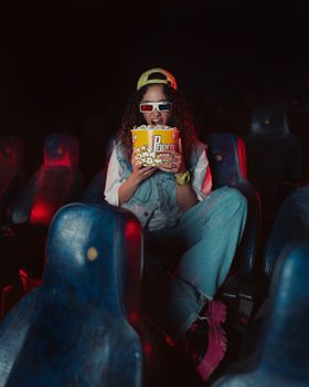 Young woman with popcorn wearing 3D glasses in a colorful movie theater.