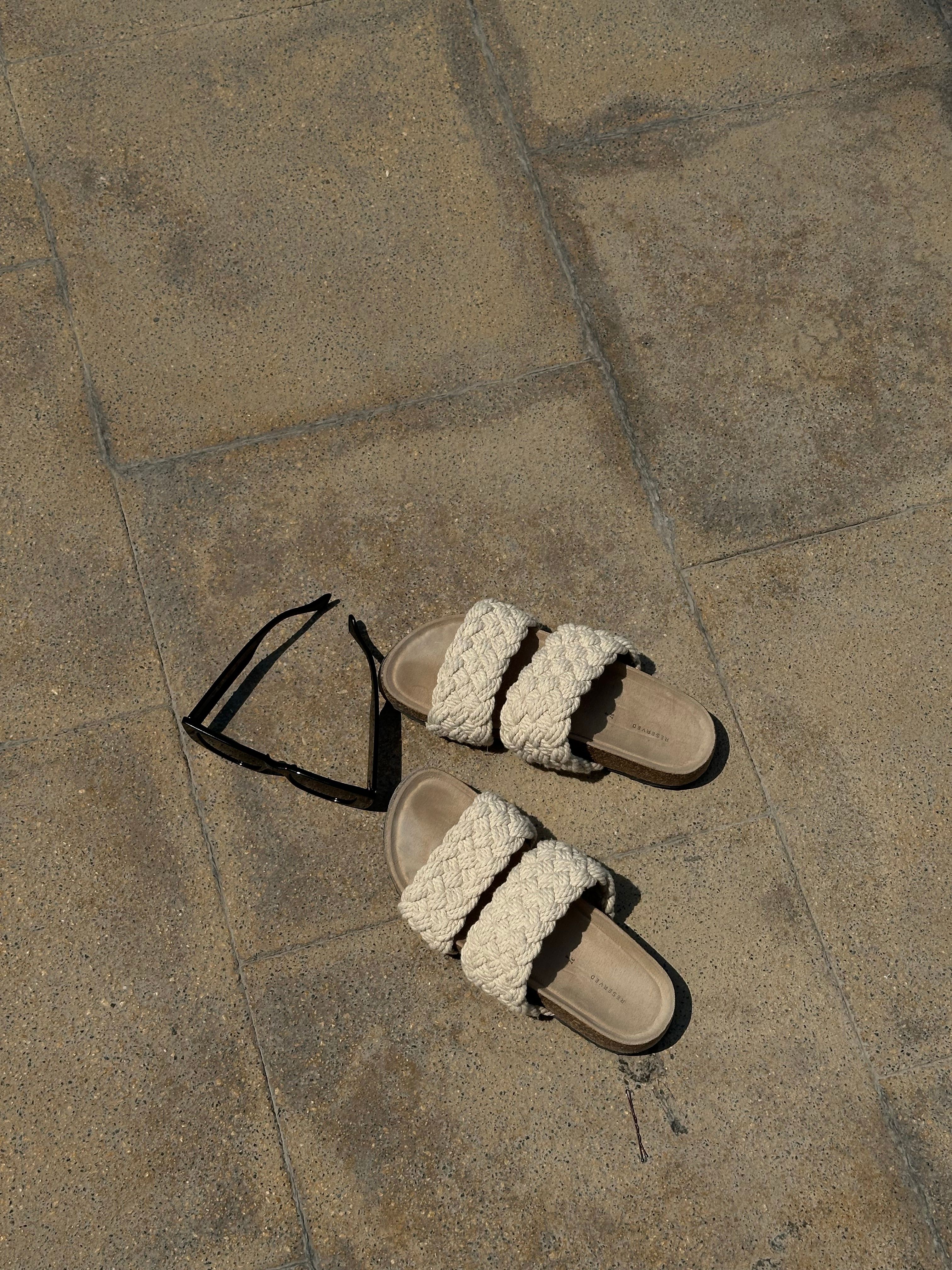 Woven sandals and sunglasses on a sunny sidewalk, capturing a summer vibe.