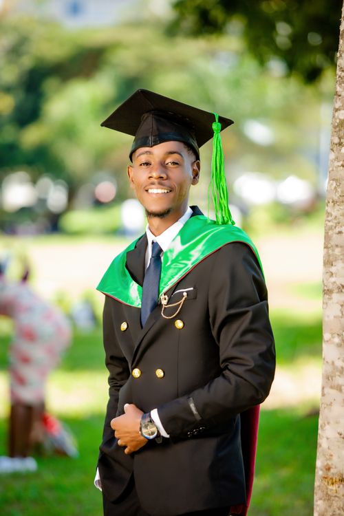 Free Smiling young graduate wearing academic cap and gown, posing outdoors on a sunny day. Stock Photo