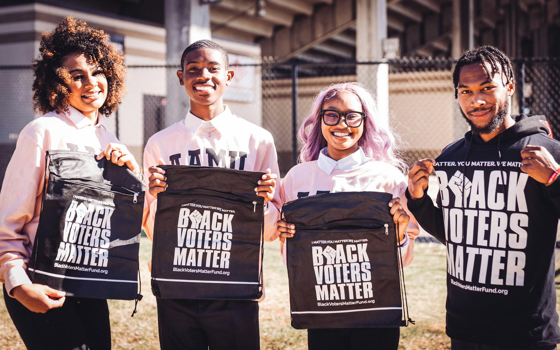 A group of young adults smiling and holding Black Voters Matter bags outdoors.