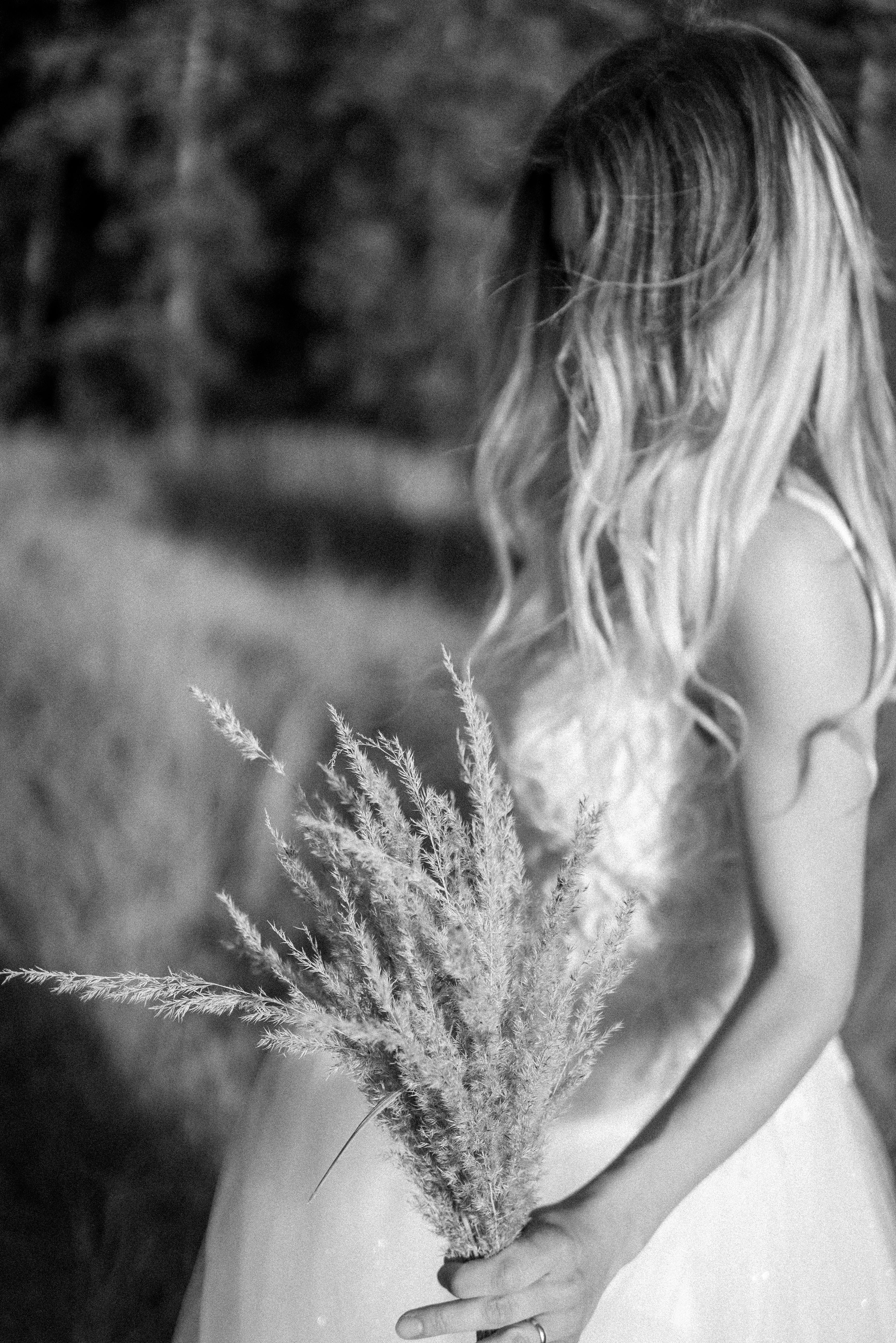 Black and white photo of a bride in nature with rustic bouquet, captured in a dreamy, rural setting.