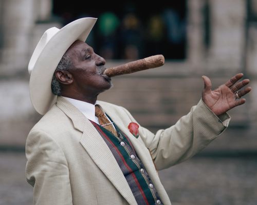 Free A senior man in a white hat and suit smokes a large cigar on a city street. Stock Photo