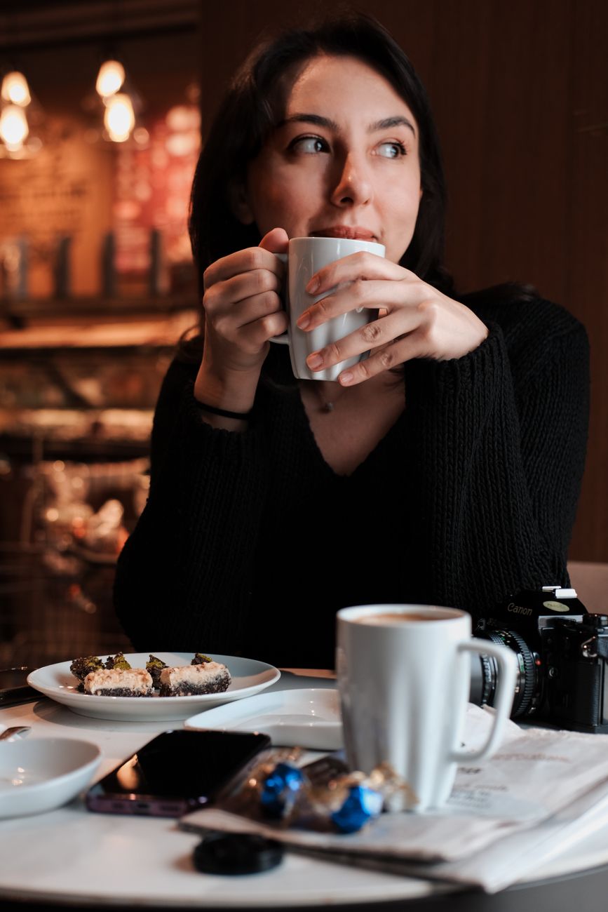 Woman enjoying coffee and dessert in a cozy cafe setting.
