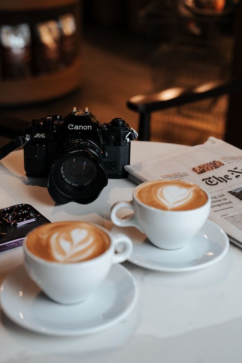Free Artistic cappuccino cups with camera setup on cozy cafe table. Stock Photo