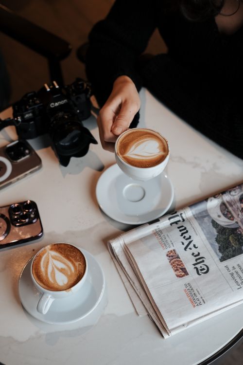 Free Two cappuccinos with leaf latte art on a table in a cafe, featuring a hand holding a cup. Stock Photo