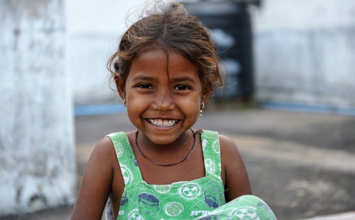 Portrait of a Little Girl in a Dress Sitting Outside and Smiling 