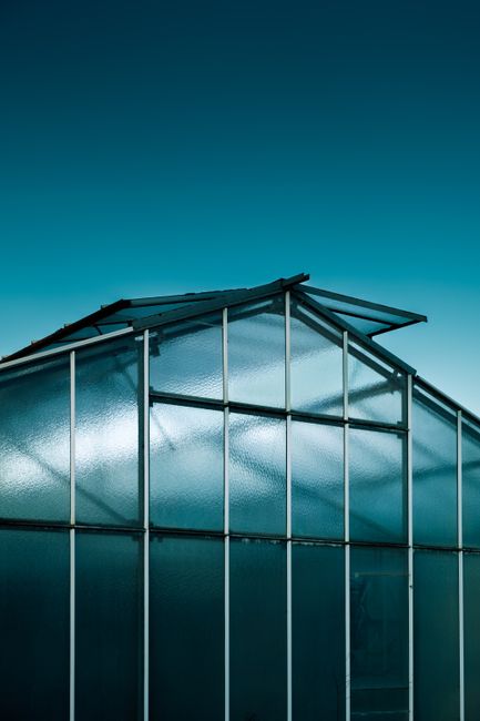 A sleek modern greenhouse is set against a vibrant blue sky, showcasing architecture and sustainability.