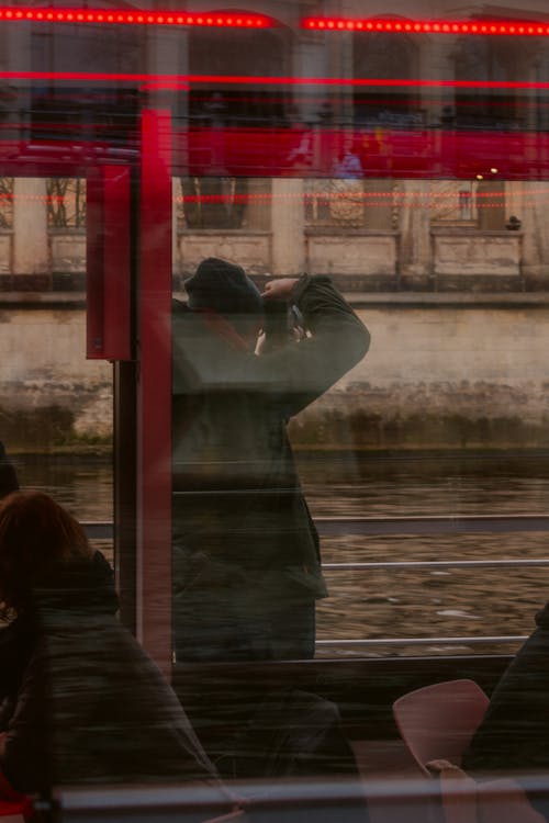 Person Standing behind Window by River and Taking Pictures