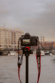 A cityscape view captured through a camera on a tripod by the river with cloudy skies.