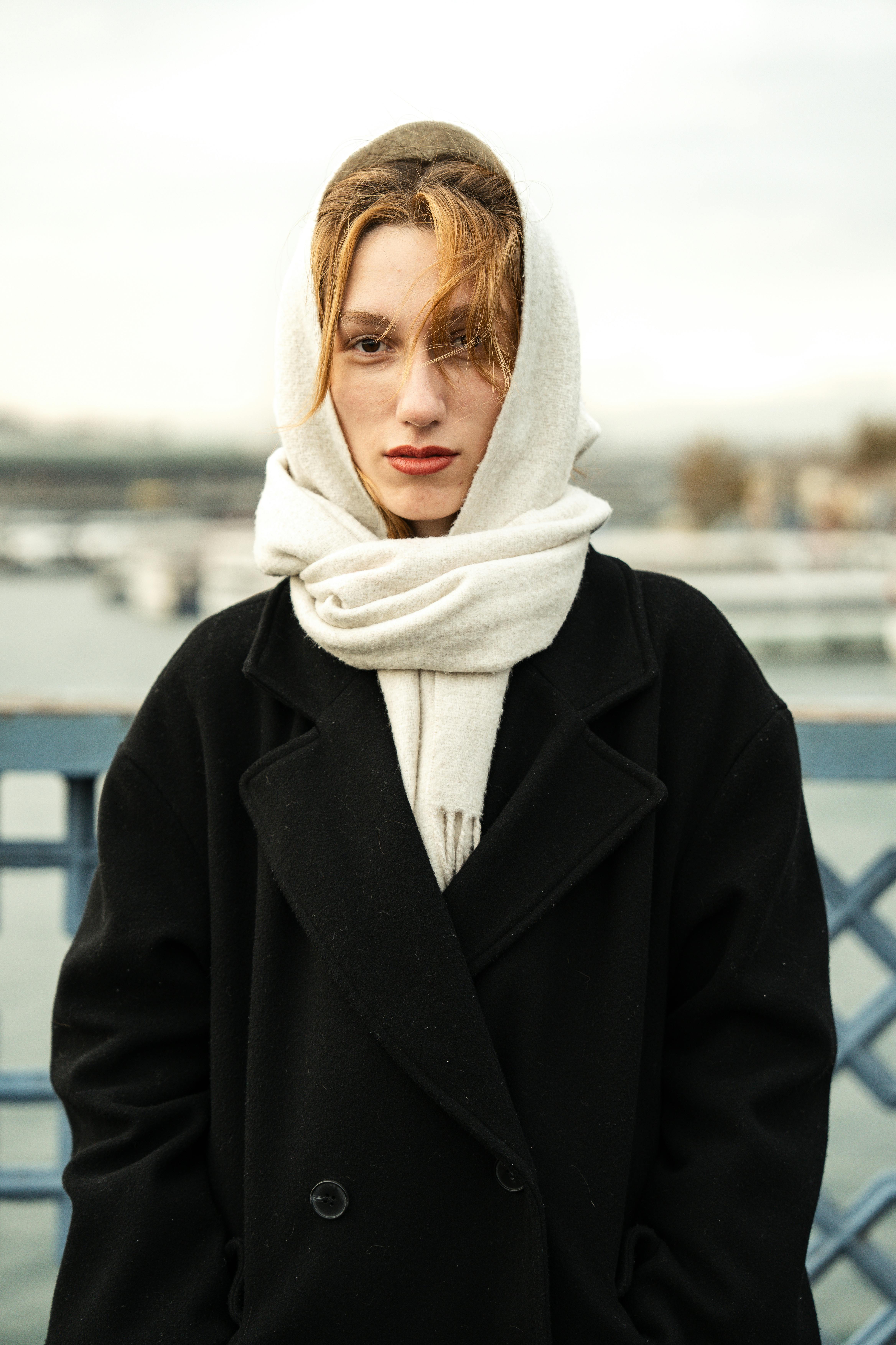 Stylish woman wearing a black coat and scarf standing outdoors on a bridge.