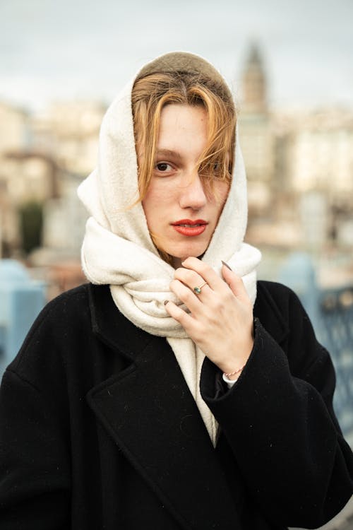 Photo of a Young Woman in a Coat and Scarf Standing in City 