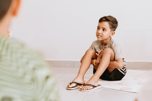 Portrait of a young boy sitting indoors on a floor mat, looking thoughtful.