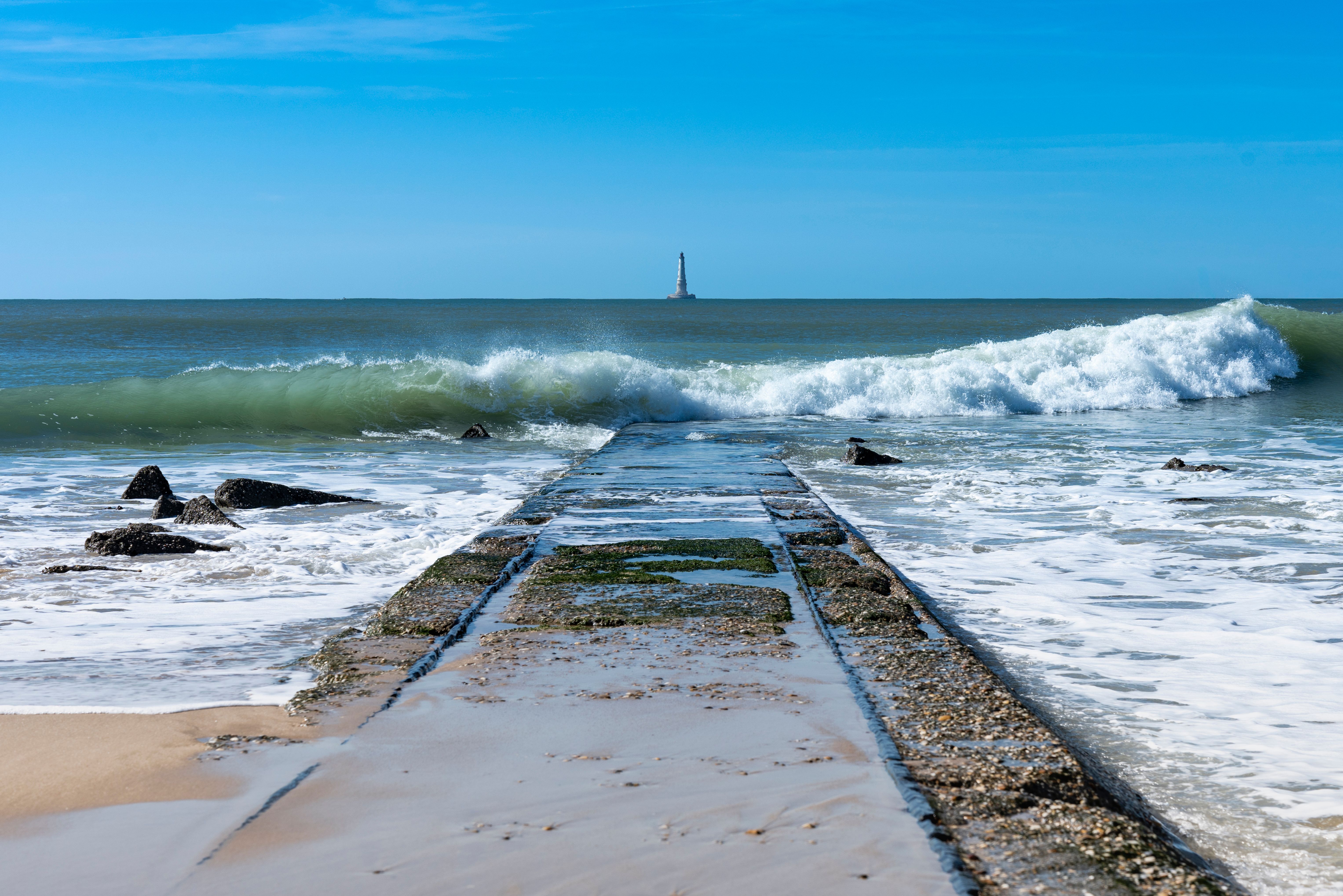 View of a Wave Washing up the Shore and a Lighthouse in Distance · Free ...