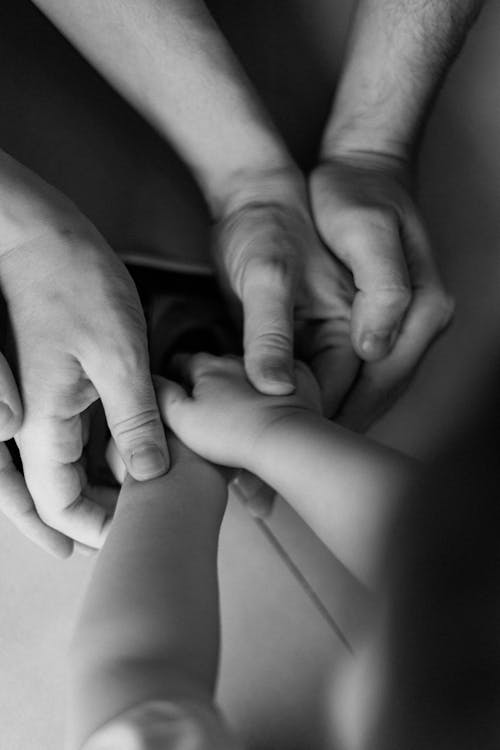 Parents Holding Hands of Their Child in Black and White 