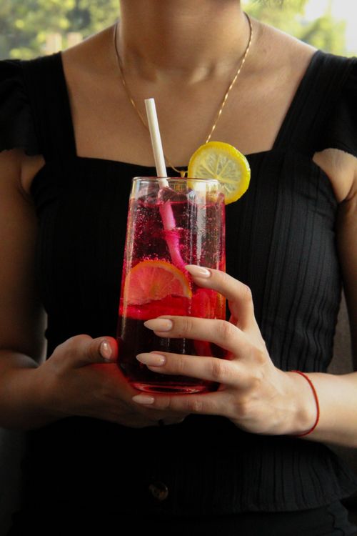 Free Bright citrus cocktail with lemon slice held by woman in black outfit, perfect for summer refreshment. Stock Photo