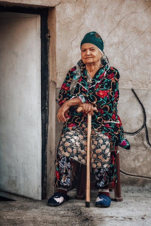 Elderly Woman with a Rod Sitting on a Street