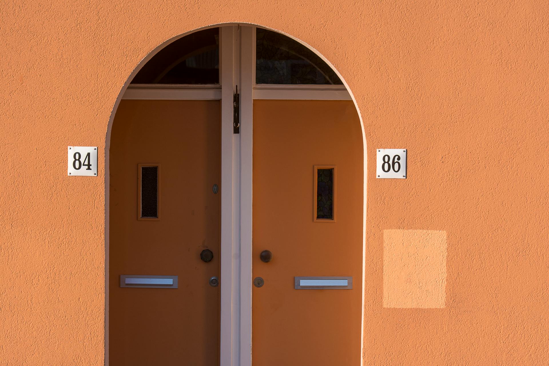 Elegant arched entrance featuring vibrant orange double doors with number plates.