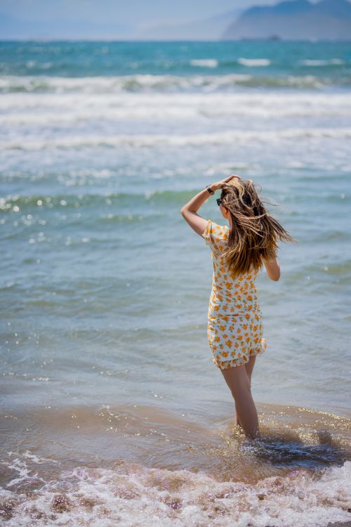 Free Rear view of woman on the shoreline, enjoying the summer waves under a bright sun. Stock Photo