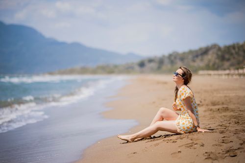 Free A woman sits on a sunny beach, enjoying the summer waves and warm sand. Stock Photo