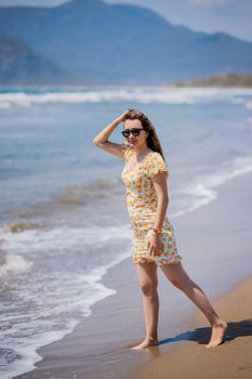 Woman wearing a floral dress enjoying a sunny day walking on the beach.