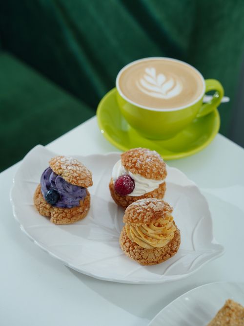 Free Delicious cappuccino with latte art paired with assorted cream puffs in a cozy cafe setting. Stock Photo