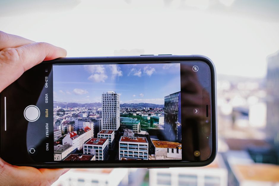 A hand holds a smartphone capturing a vibrant cityscape under a clear blue sky.