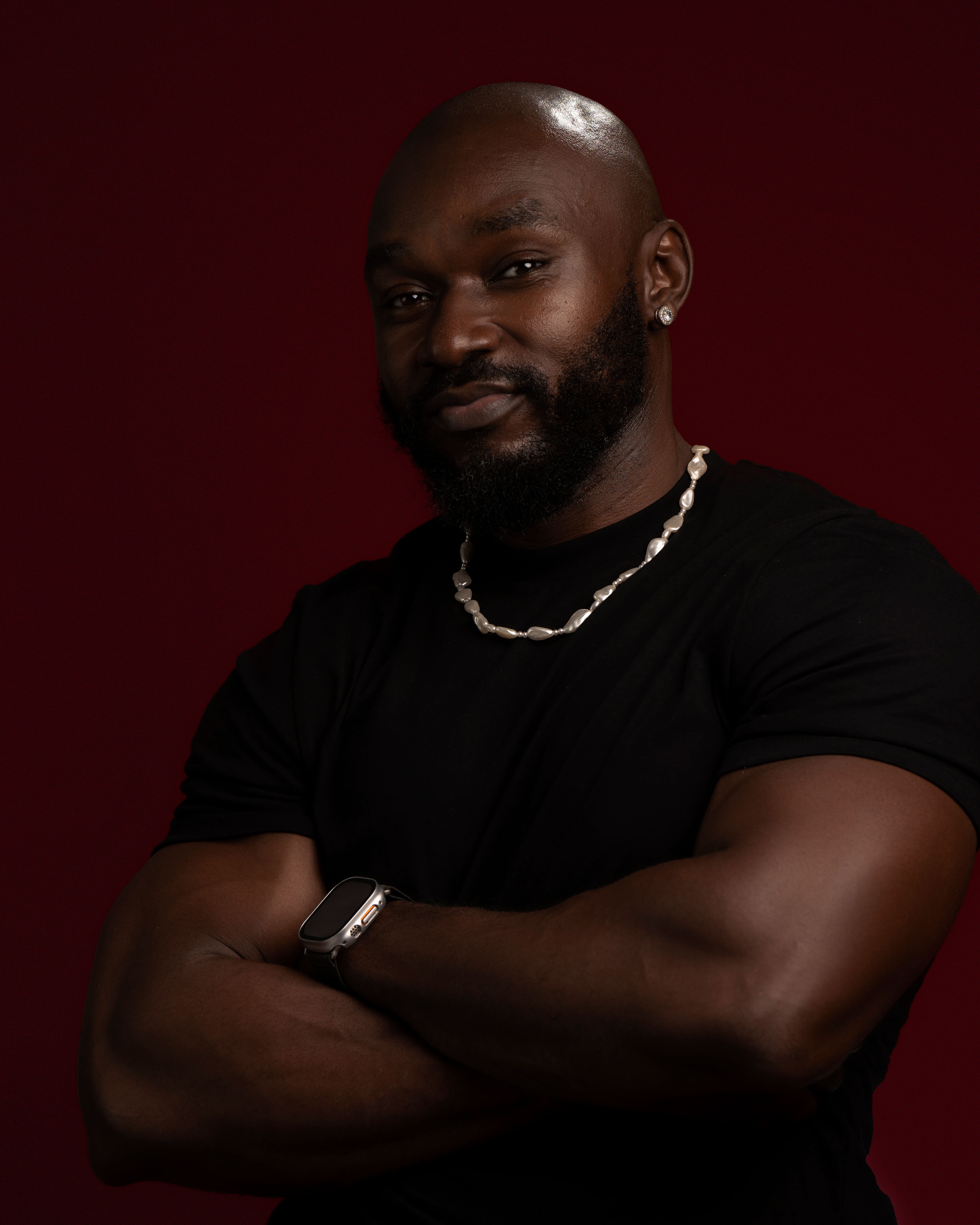 Studio portrait of a confident bald man with a beard, wearing a black t-shirt against a dark background.