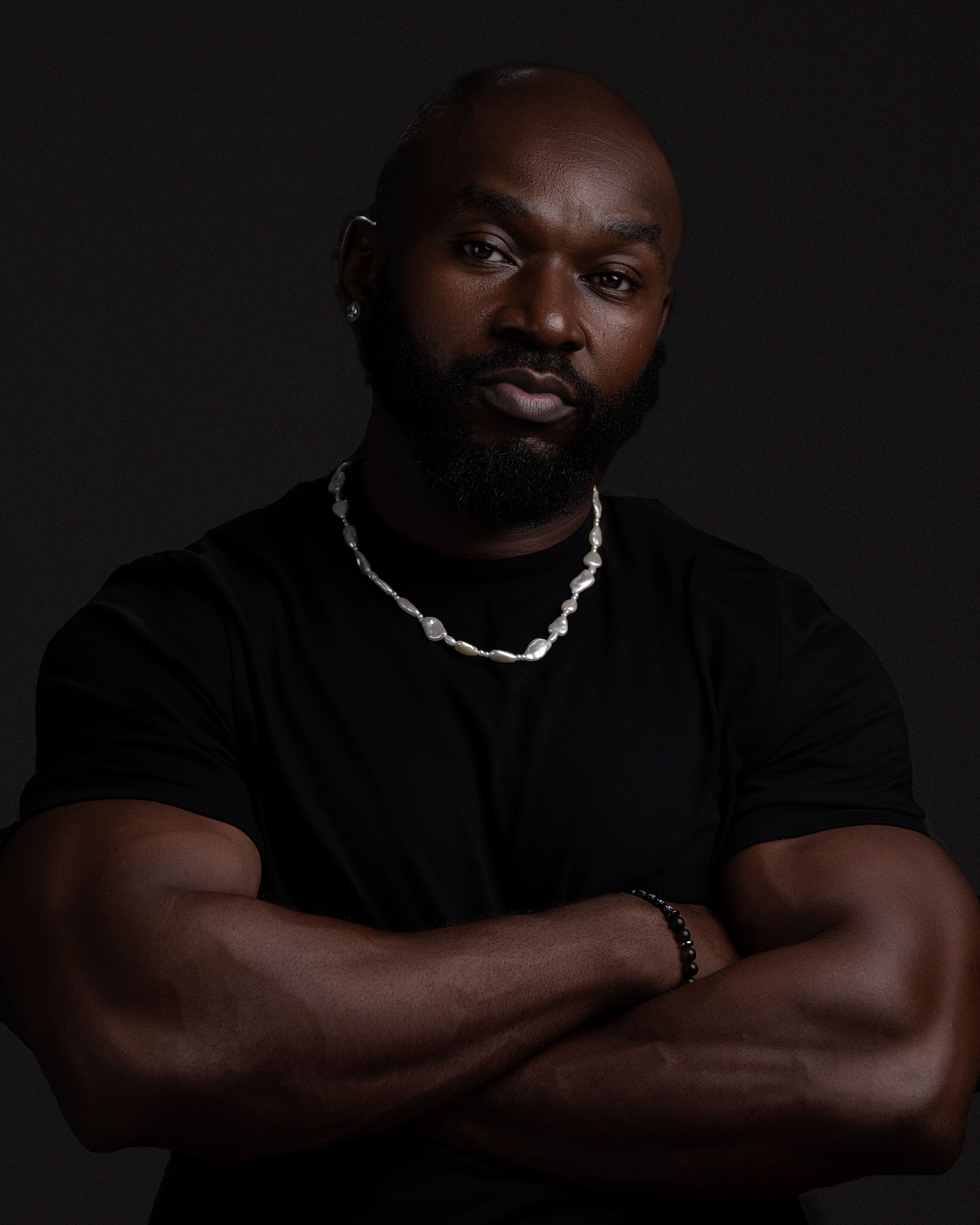 A muscular man with a beard poses confidently in a dark studio setting, displaying strength and determination.