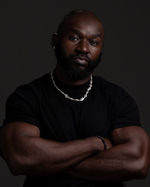 Dark Studio Shot of a Bearded Muscular Man Standing with Arms Crossed 