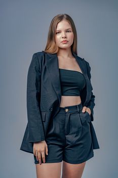Portrait of a confident woman in a modern dark outfit posing against a plain background.