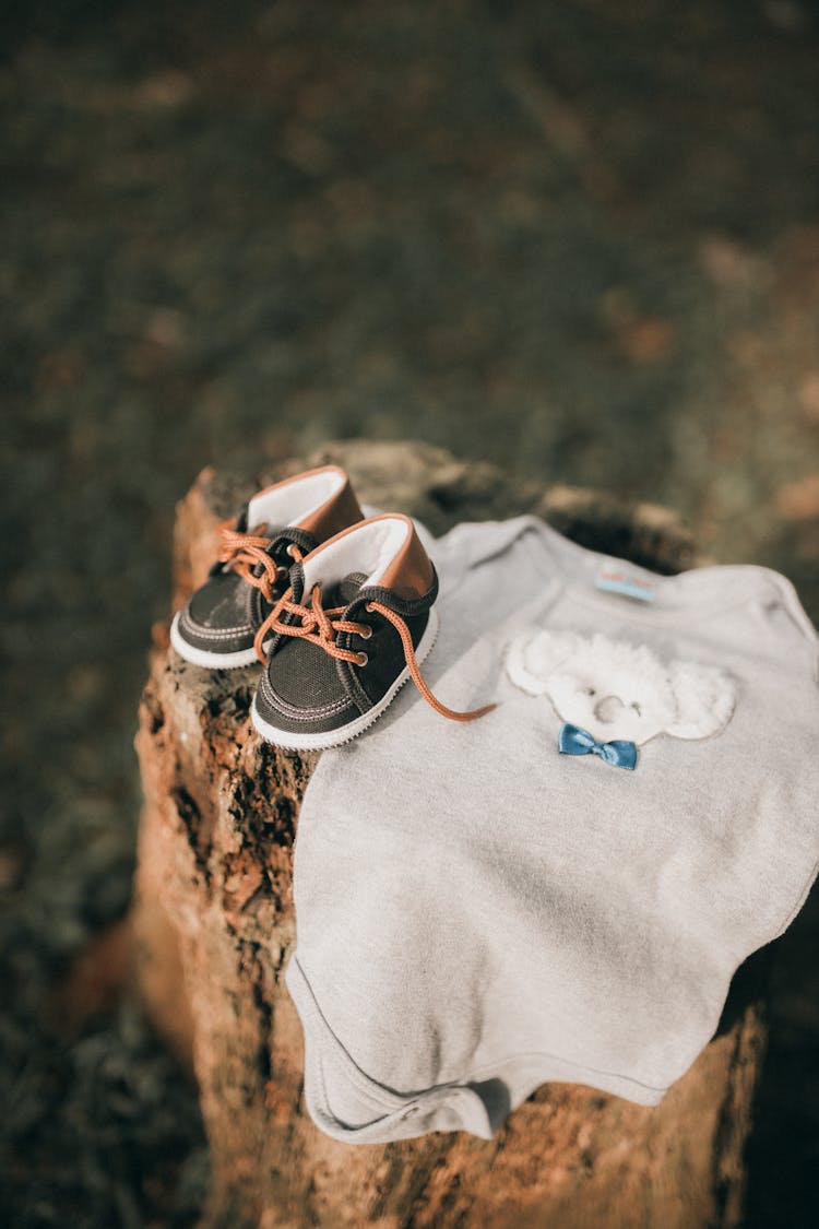 Baby Bodysuit And Pair Of Shoes On Tree Trunk