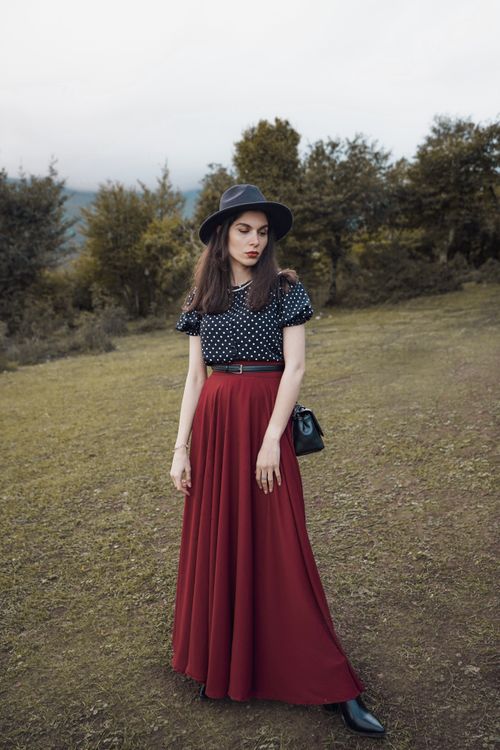 Free Woman in red skirt and black spotted shirt posing in a rural meadow. Stock Photo