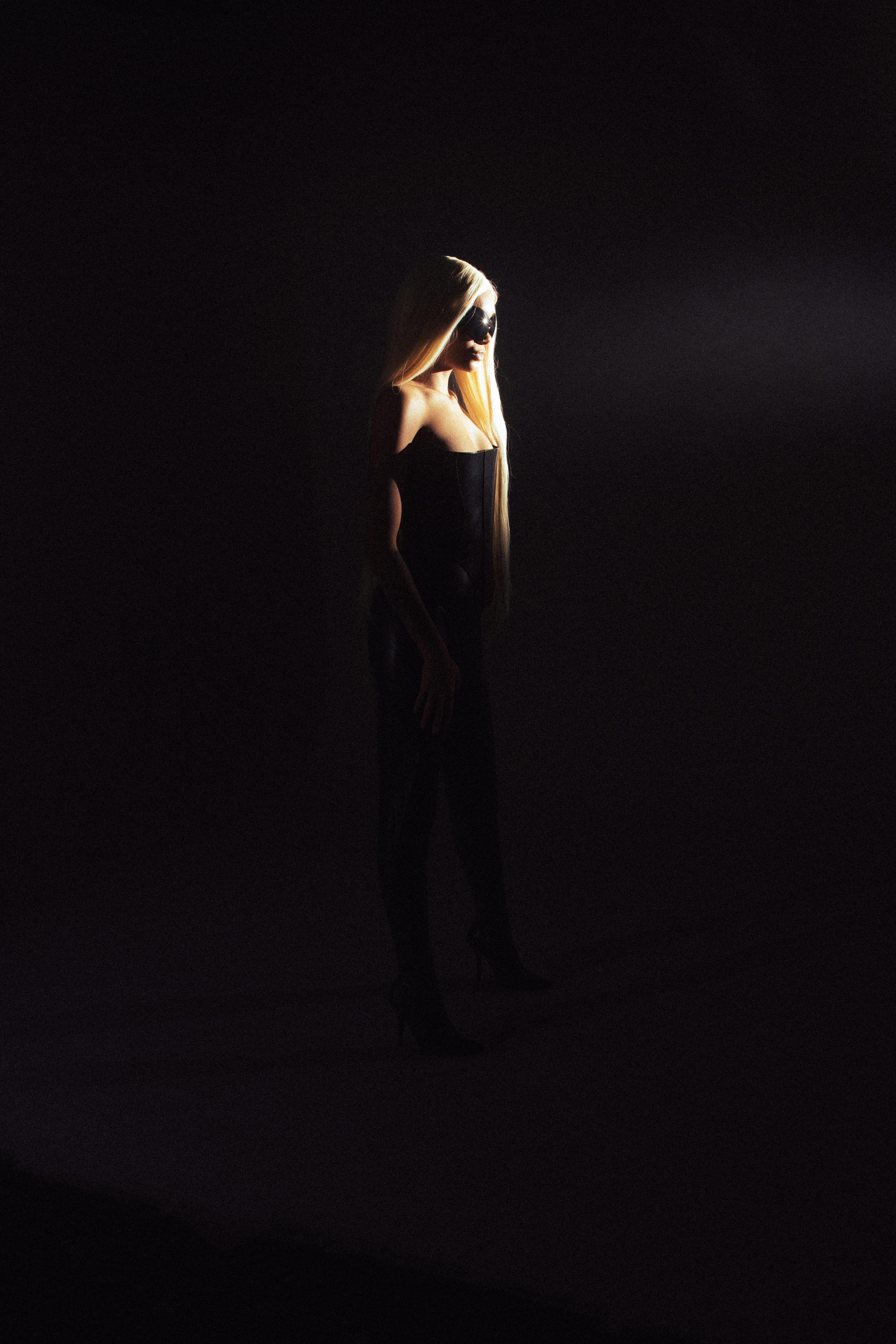 A dramatic fashion portrait of a woman in darkness with spotlight highlighting her silhouette.