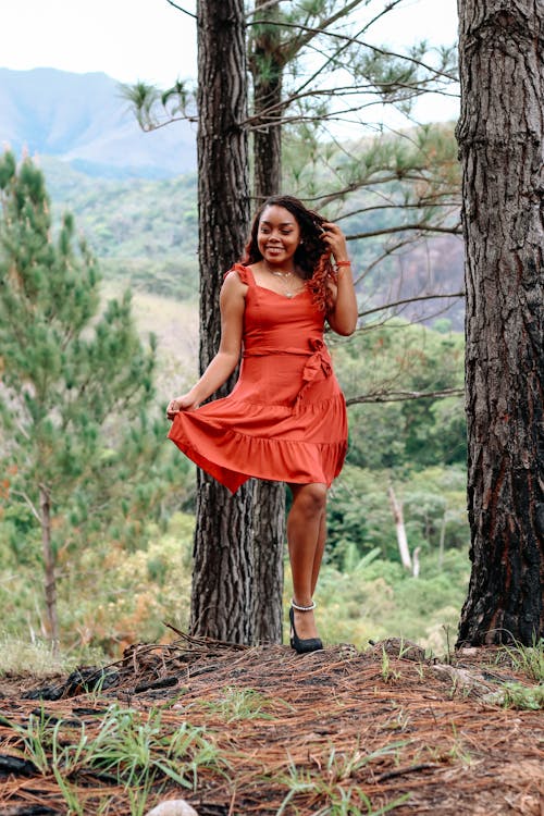 Young Woman in a Red Dress Standing by the Tree in a Forest 