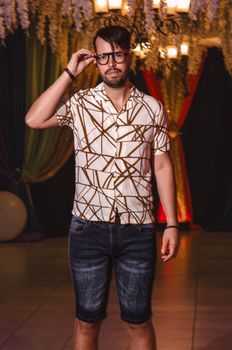 Fashionable man in a geometric shirt and glasses posing indoors. Casual yet trendy look.