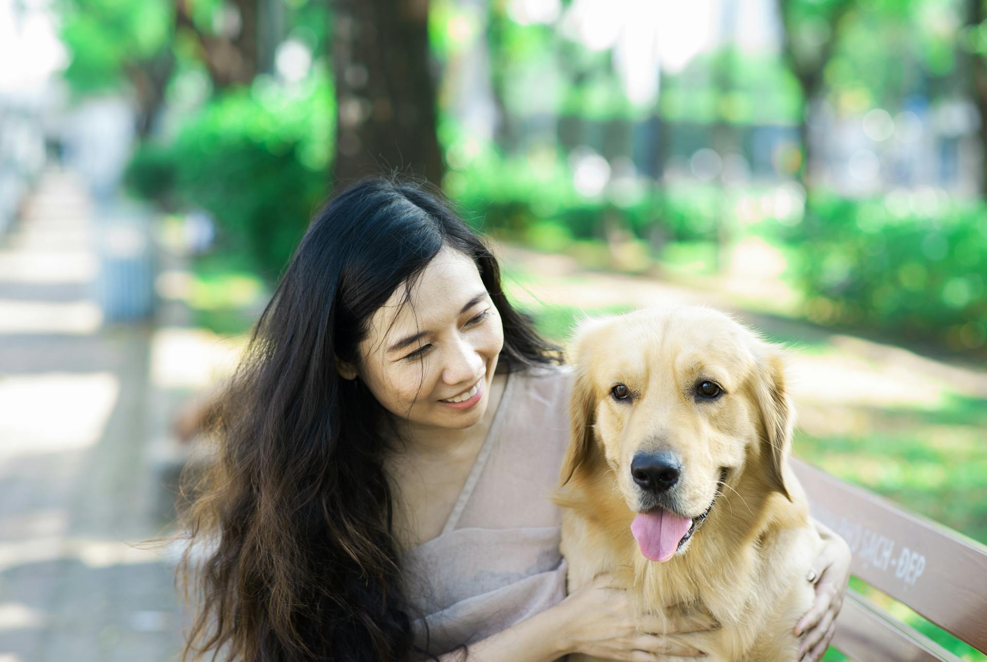 Woman Sitting on a Bench in a Park with Her Dog and Smiling