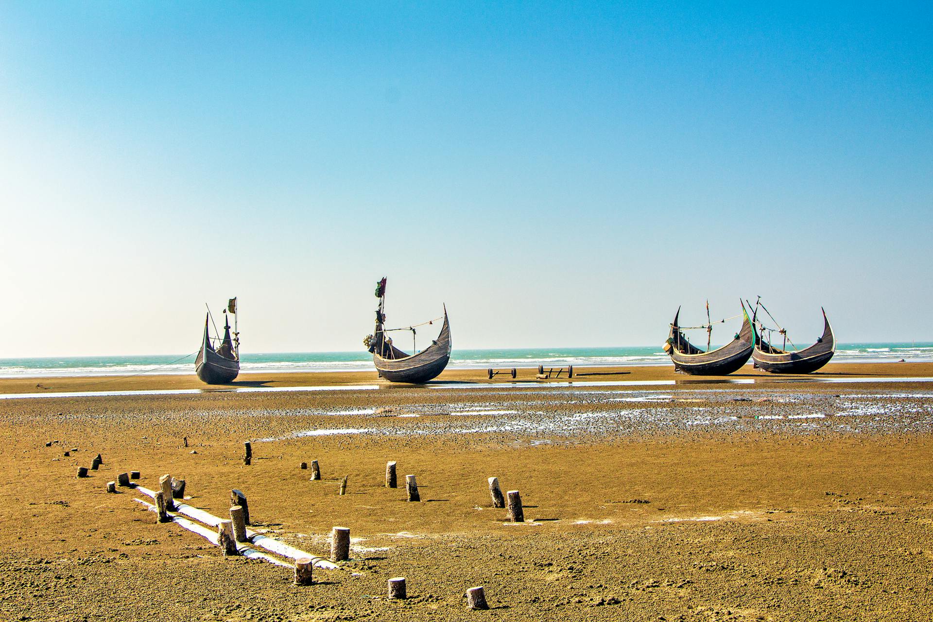 Traditional wooden boats on the sandy shores of Cox's Bazar, Bangladesh under a clear blue sky.