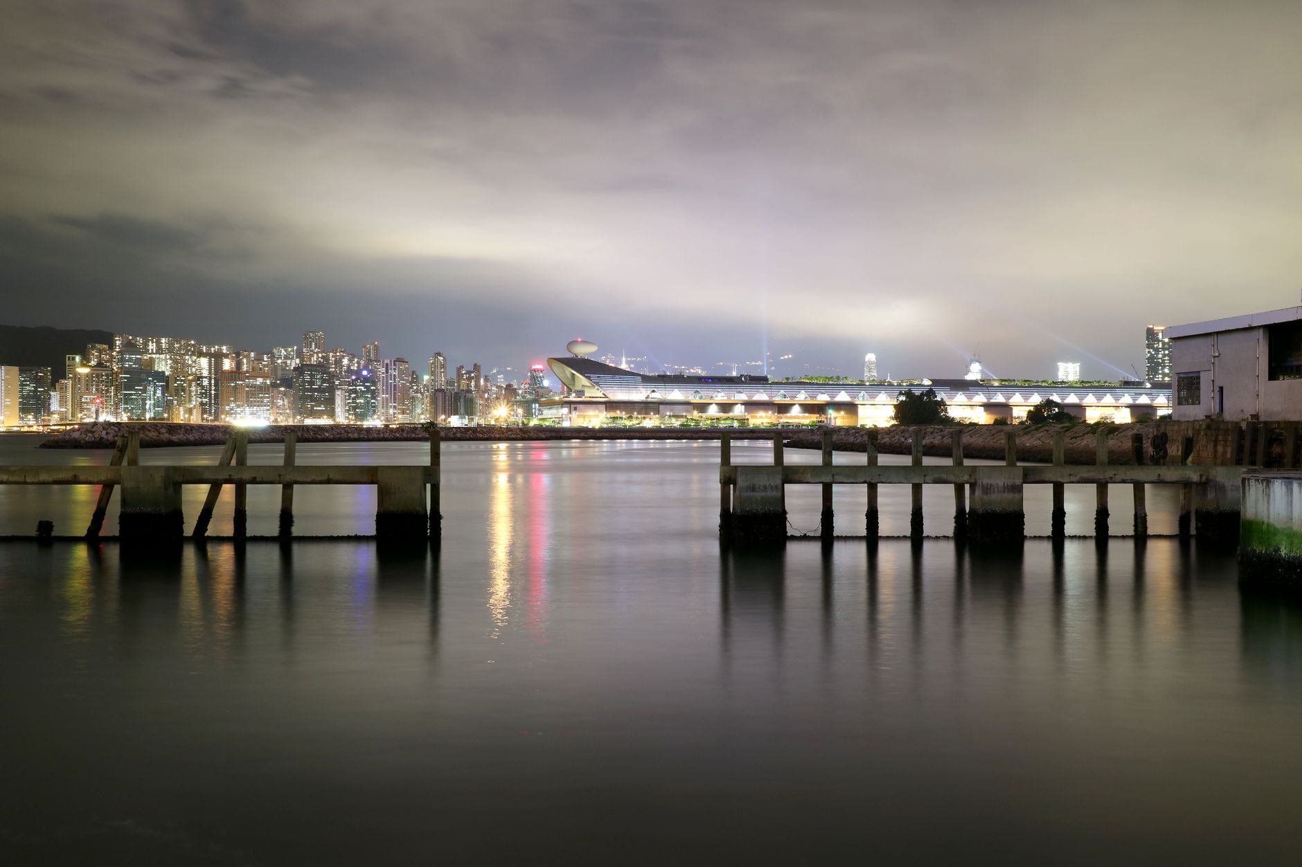 Hong Kong Island waterfront cityscape at night with a bridge reflecting in the water.